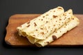 Homemade Norwegian Potato Flatbread Lefse with Butter and Sugar on a rustic wooden board on a black surface, side view. Close-up