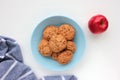 Homemade oatmeal cookies in a blue bowl and red apple on white table.Flat lay composition with oat biscuits, fresh fruit