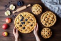 Homemade organic apple pies bakery products hold female hands on dark wooden kitchen table with raising, bluberry