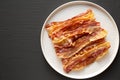 Homemade Oven Baked Bacon on a  Plate on a black surface, top view. Flat lay, overhead, from above. Copy space Royalty Free Stock Photo