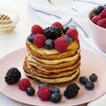 Homemade pancakes with berries and honey on a pink plate over white wooden surface, side view. Close-up Royalty Free Stock Photo