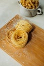 Homemade Pappardelle raw pasta on wooden board in bright kitchen. raw tortiglioni pasta on background in cup. process of making