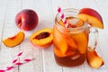 Homemade peach iced tea in a mason jar glass with a white wood background