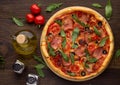Homemade pizza with ham, tomatoes, olives and arugula on dark wooden table. Royalty Free Stock Photo