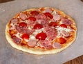 Homemade pizza prepared for baking with sausage and tomatoes on a baking paper