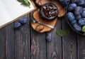 Homemade plum jam in a glass jar and fresh blue plums in a bowl on a dark rustic wooden background with copy space top view.