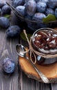 Homemade plum jam in a glass jar and fresh blue plums in a bowl on a dark rustic wooden background with copy space top view. Royalty Free Stock Photo