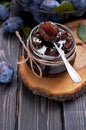 Homemade plum jam in a glass jar and fresh blue plums in a bowl on a dark rustic wooden background with copy space top view.