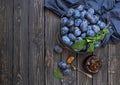 Homemade plum jam in a glass jar and fresh blue plums in a bowl on a dark rustic wooden background with copy space top view.