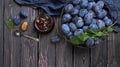 Homemade plum jam in a glass jar and fresh blue plums in a bowl on a dark rustic wooden background with copy space top view.