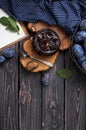 Homemade plum jam in a glass jar and fresh blue plums in a bowl on a dark rustic wooden background with copy space top view.