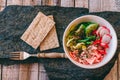 Homemade poke bowl from ham, cucumber, radish, sunflower seed, fork and cracker on stone