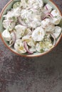 Homemade potato salad with pickles, dill and red onion with creme fraiche dressing close-up in a plate. Vertical top view