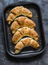 Homemade puff pastry walnuts brown sugar croissants on a baking sheet on a dark background, top view