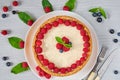 Homemade raspberry cheesecake on the white plate decorated with fresh berries, mint leaves, knife and fork on the gray table Royalty Free Stock Photo