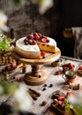 Homemade raspberry sliced biscuit cake with white cream and berries on top on wooden cake stand