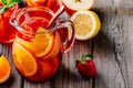 Homemade red wine sangria with orange, apple, strawberry and ice in pitcher and glass on wooden background