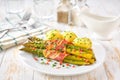 Homemade roasted bundles of green asparagus wrapped in bacon on a ceramic plate on a white wooden table, close up Royalty Free Stock Photo