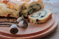 Homemade roll with poppy seeds on round wooden board background. Slices of cake