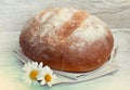 Homemade round bread on cloth with daisies on wood.