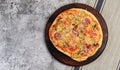 Homemade rustic pizza with pickled cucumbers, cheese and mushrooms on a round wooden cutting board on a dark grey background Royalty Free Stock Photo