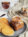 Homemade salted caramel sauce in a glass jar on a rustic wooden table. Close-up. Round caramel poured wafers in the foreground. Royalty Free Stock Photo