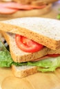 Homemade sandwich breakfast preparing. Close up whole wheat sandwich bread with slice tomatoes and lettuce stacked on wooden cutti Royalty Free Stock Photo