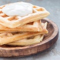 Homemade savory belgian waffles with bacon and shredded cheese, served with plain yogurt on a wooden plate, square