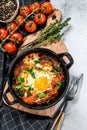 Homemade shakshuka, fried eggs, onion, bell pepper, tomatoes and parsley in a pan. Gray background. Top view