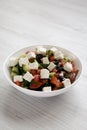 Homemade Shepards salad with cucumbers, parsley and feta in a white bowl on a white wooden table, side view. Close-up