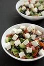 Homemade Shepherd`s salad with cucumbers, parsley and feta in white bowls on a black surface, low angle view. Selective focus