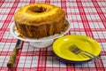 Homemade simple cake on white stand on table with white and red checkered tablecloth. Homemade common cake in front view