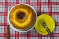 Homemade simple cake with yellow dish next to it on table with white and red checkered tablecloth. Homemade common cake in top vie