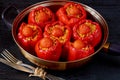 Homemade stuffed red bell peppers with rice and vegetables in a vintage frying pan on the black background