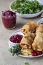Homemade stuffed thin pancakes or crepes with meat, spicy cranberry sauce and arugula, light stone background. Traditional Russian