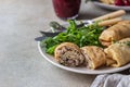 Homemade stuffed thin pancakes or crepes with meat, spicy cranberry sauce and arugula, light stone background. Traditional Russian