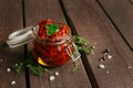 Homemade sun-dried tomatoes in oil with fresh herbs thyme, oregano in a glass jar on dark wooden background Royalty Free Stock Photo