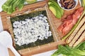 Homemade sushi food preparation with Nori algea sheet with rice on bamboo mat and ingredients like smoked salmon, avocado and egg