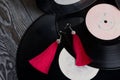 Homemade tassel earrings in red. Against the background of old vinyl records and brushed pine boards painted in black and white Royalty Free Stock Photo