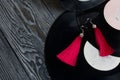 Homemade tassel earrings in red. Against the background of old vinyl records and brushed pine boards painted in black and white Royalty Free Stock Photo