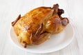 Homemade tasty rotisserie chicken on white plate on a white wooden background, side view. Close-up Royalty Free Stock Photo