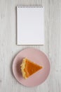 Homemade Thanksgiving pumpkin pie on a pink plate, blank notebook on a white wooden surface, top view. Overhead, from above, flat Royalty Free Stock Photo
