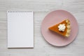 Homemade Thanksgiving pumpkin pie on a pink plate, blank notepad on a white wooden surface, overhead view. Top view, from above, Royalty Free Stock Photo