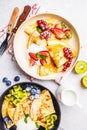 Homemade thin crepes served with curd cream, fruits and berries in black and white plates, top view Royalty Free Stock Photo