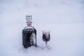 Homemade tincture of red cherry in a glass bottle and a wine crystal glass on a snow and white background Royalty Free Stock Photo