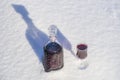 Homemade tincture of red cherry in a glass bottle and a wine crystal glass on a snow and white background Royalty Free Stock Photo