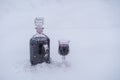 Homemade tincture of red cherry in a glass bottle and a wine crystal glass on a snow and white background Royalty Free Stock Photo