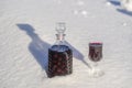 Homemade tincture of red cherry in a glass bottle and a wine crystal glass on a snow and white background Royalty Free Stock Photo