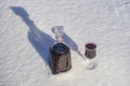 Homemade tincture of red cherry in a glass bottle and a wine crystal glass on a snow and white background Royalty Free Stock Photo