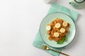 Homemade tiny cereal pancakes with banana on white table. View from above. Copy space